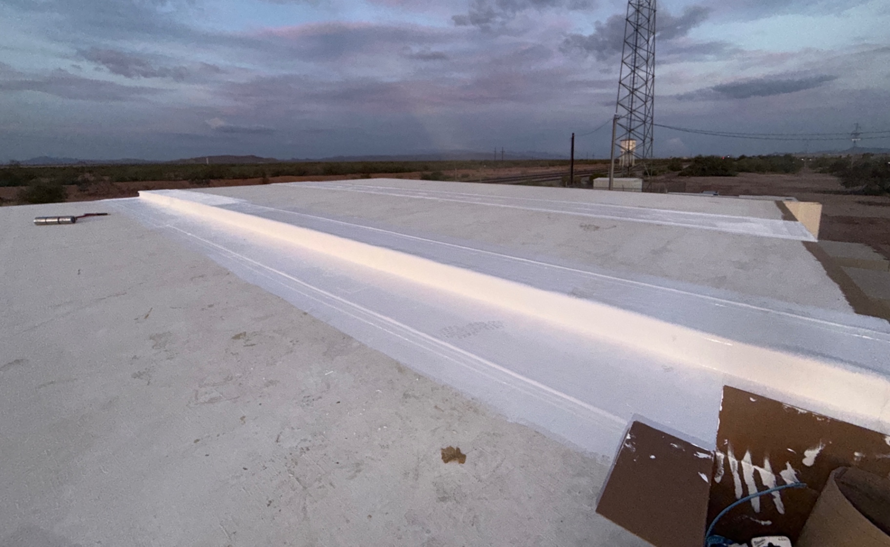 Freshly applied white roof coating on a commercial facility roof at dusk, with a communications tower behind.