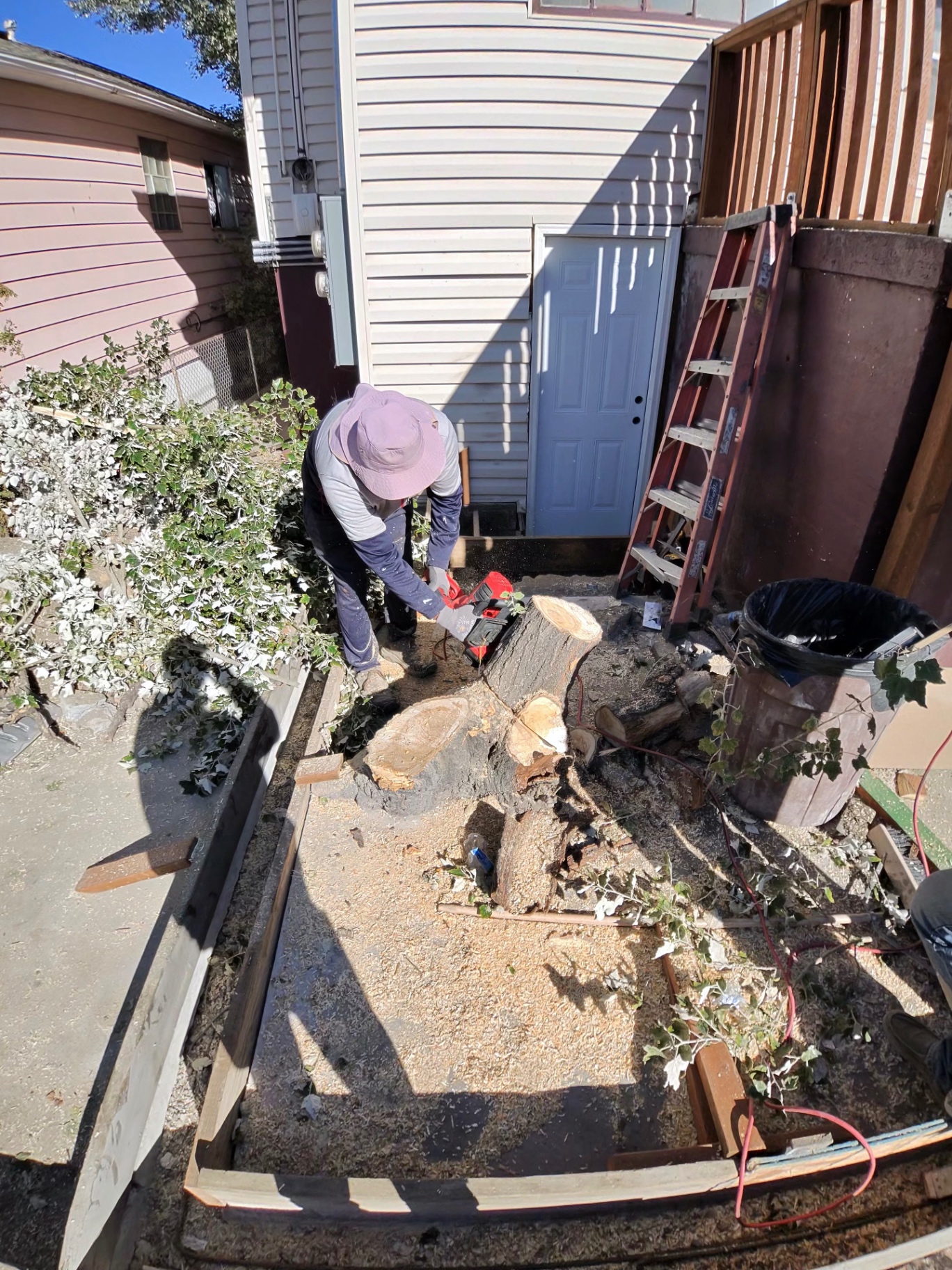 Crew member cutting up a felled tree trunk during yard clearing beside a home.