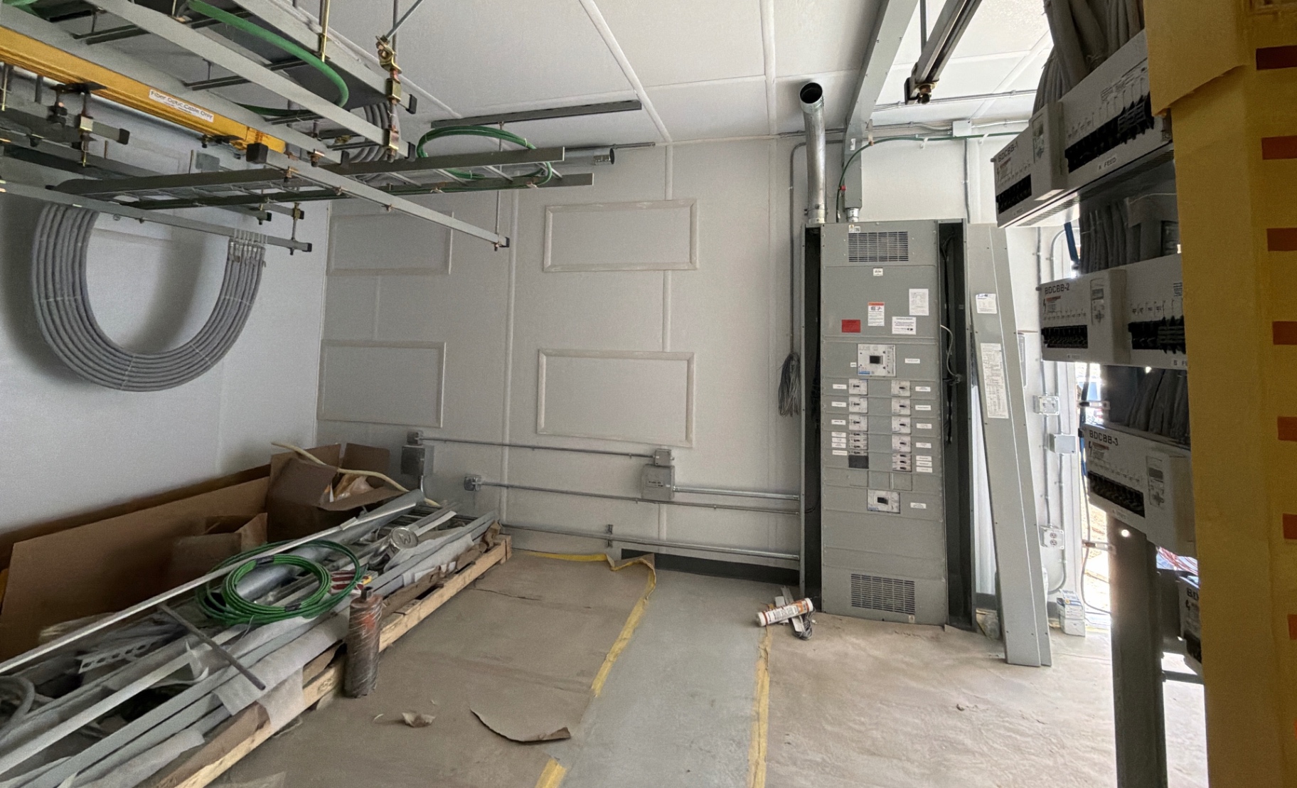 Facility room during construction support, with conduit, cable tray and equipment installed by other trades visible in the work area.