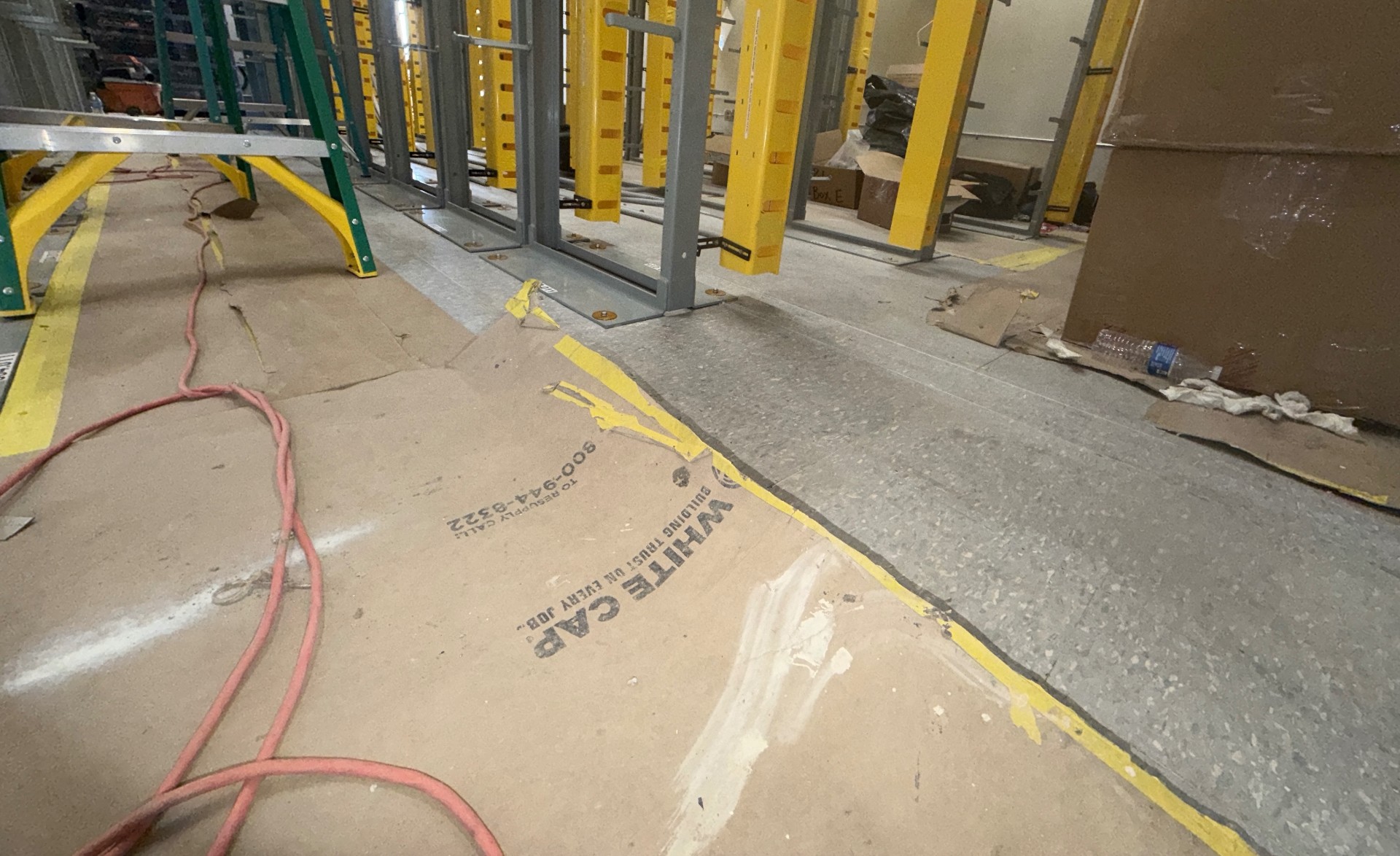 Interior concrete floor prepared and protected during facility construction support, with equipment installed by other trades visible nearby.