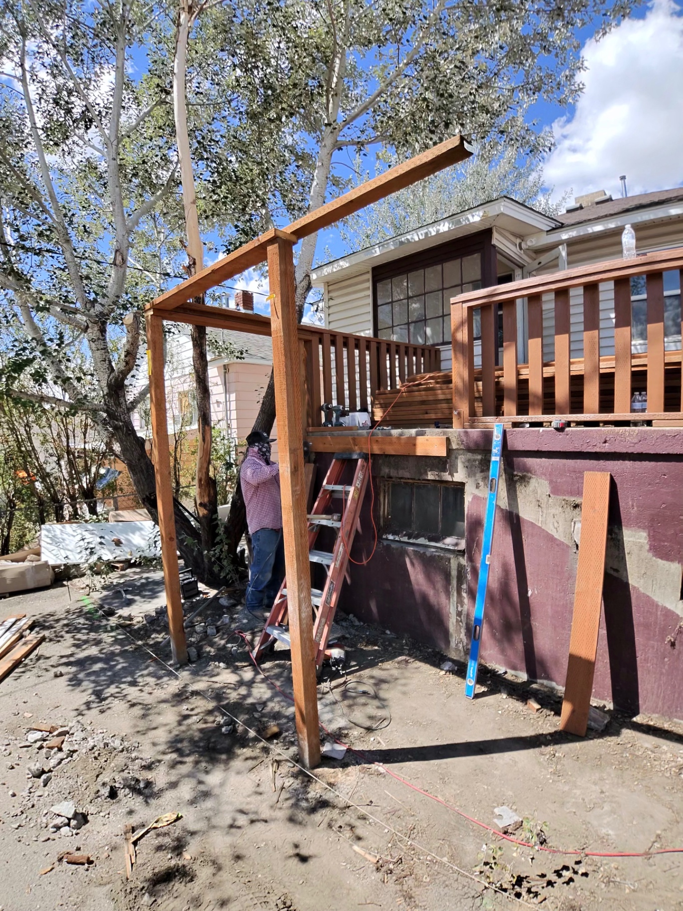Crew member setting new posts and beams for a rebuilt deck structure behind a home.