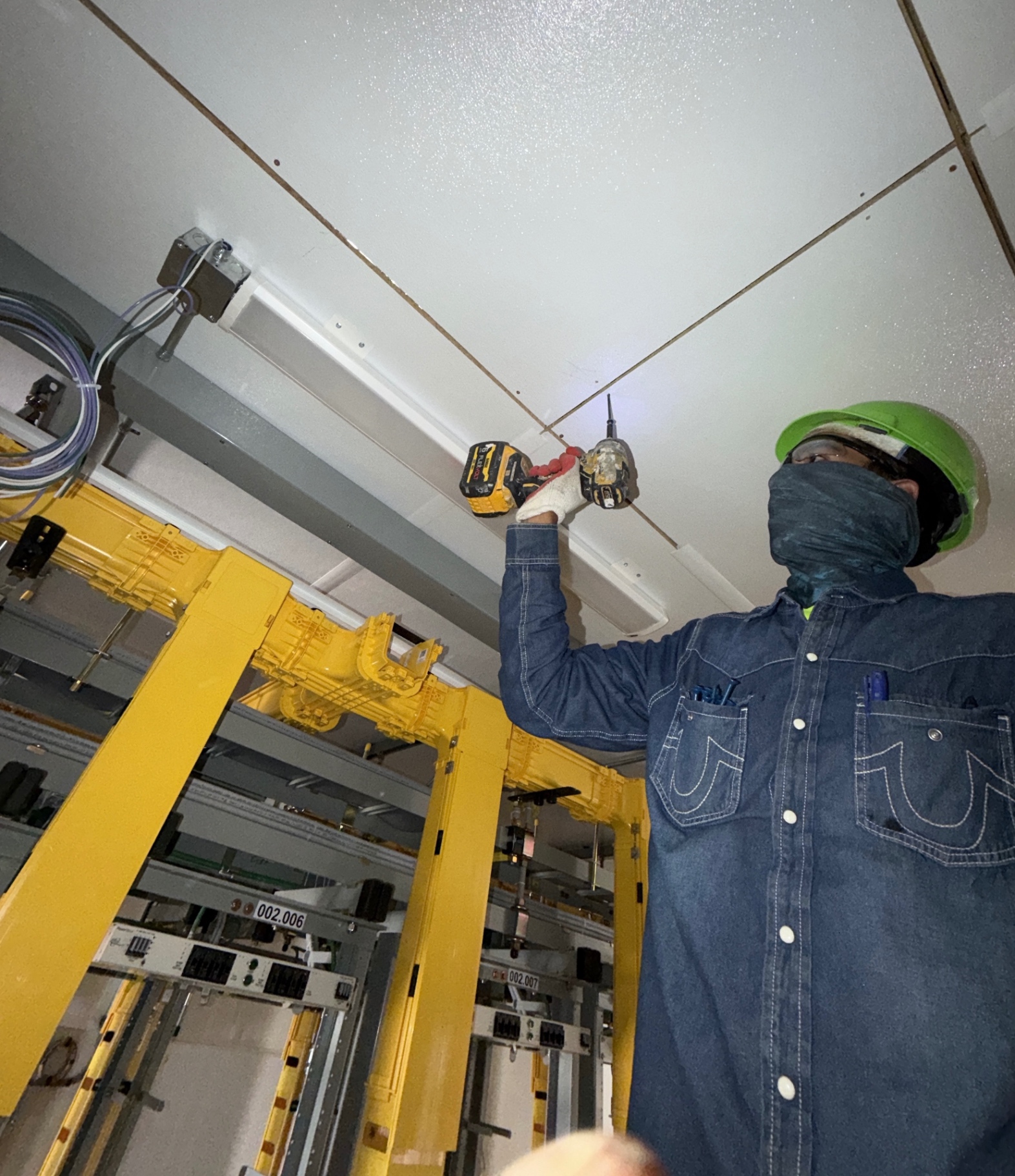 Crew member working overhead at a ceiling grid inside an equipment room during facility construction.