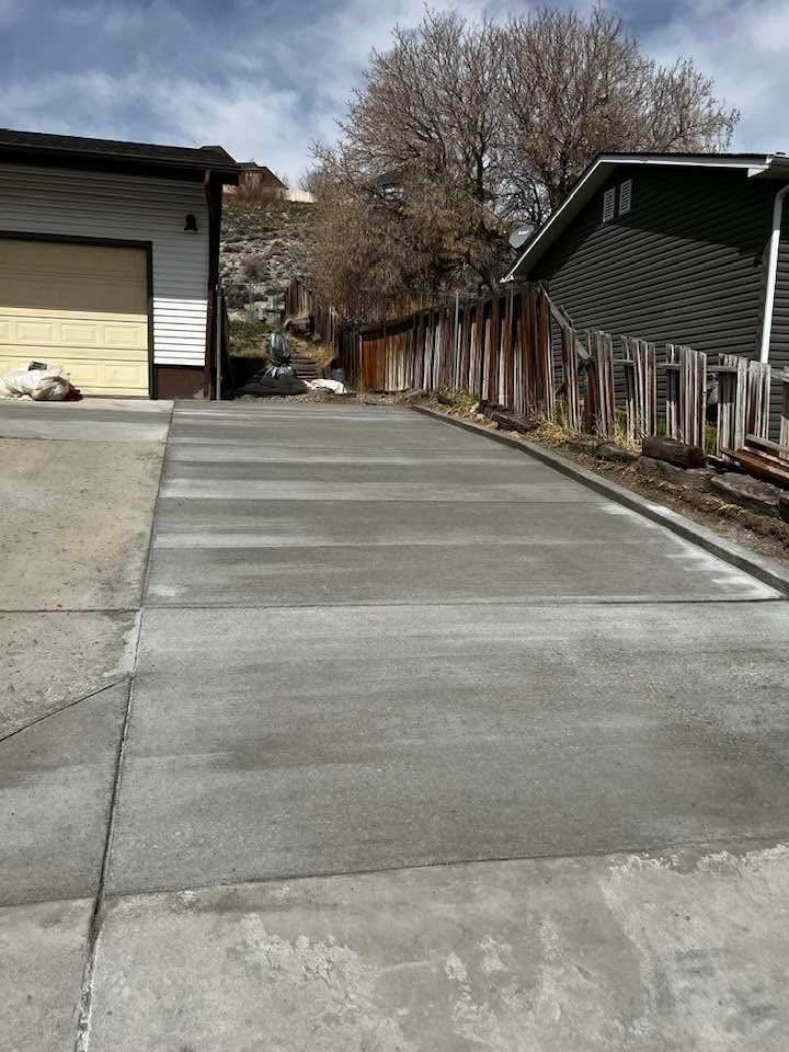 New concrete driveway running between a garage and a fence line.