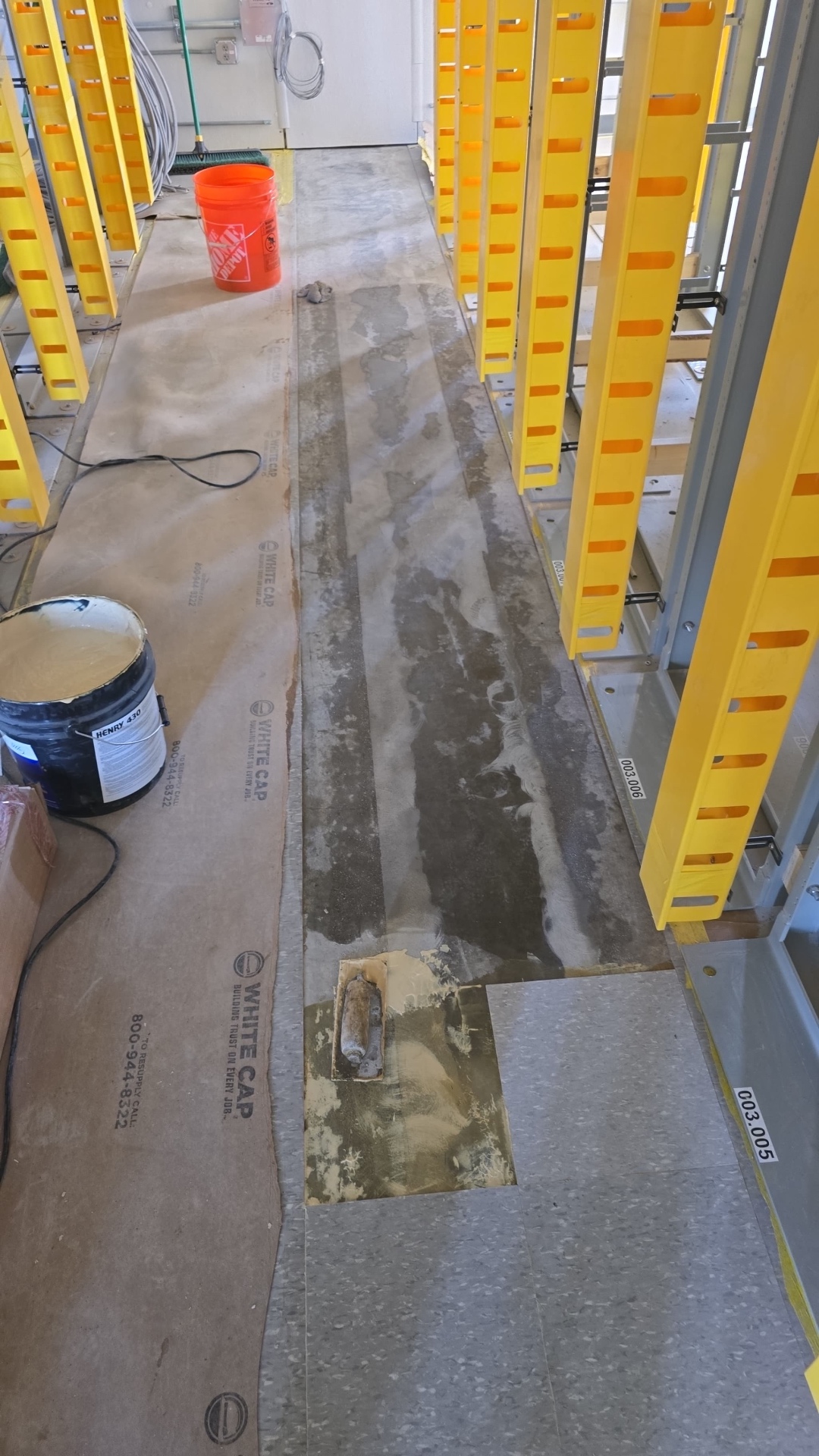 Interior concrete floor patch in progress inside a working facility, with equipment installed by other trades visible nearby.