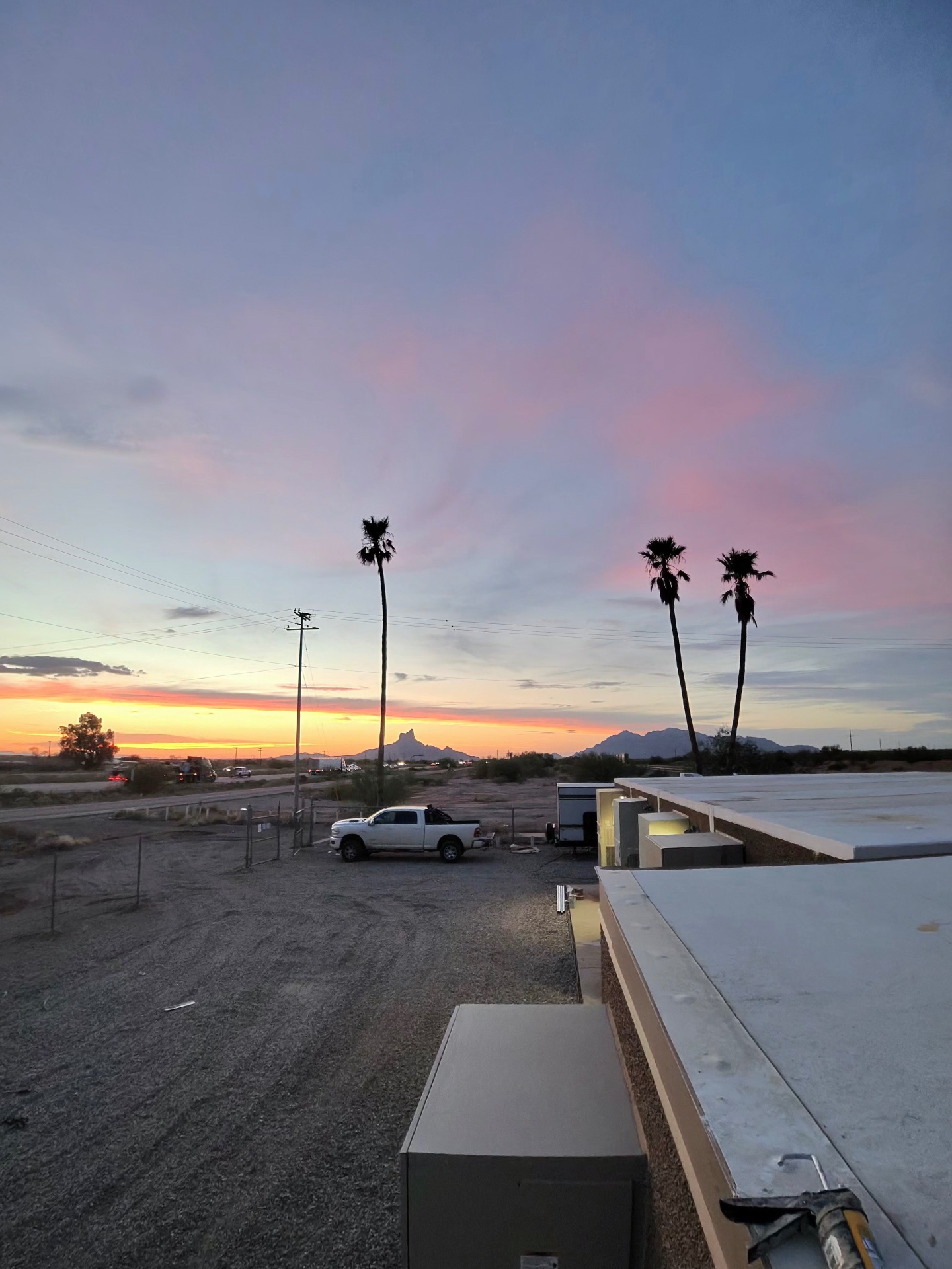 Wide dusk view across a facility site from a finished roof edge, with a work truck parked on the graded lot.