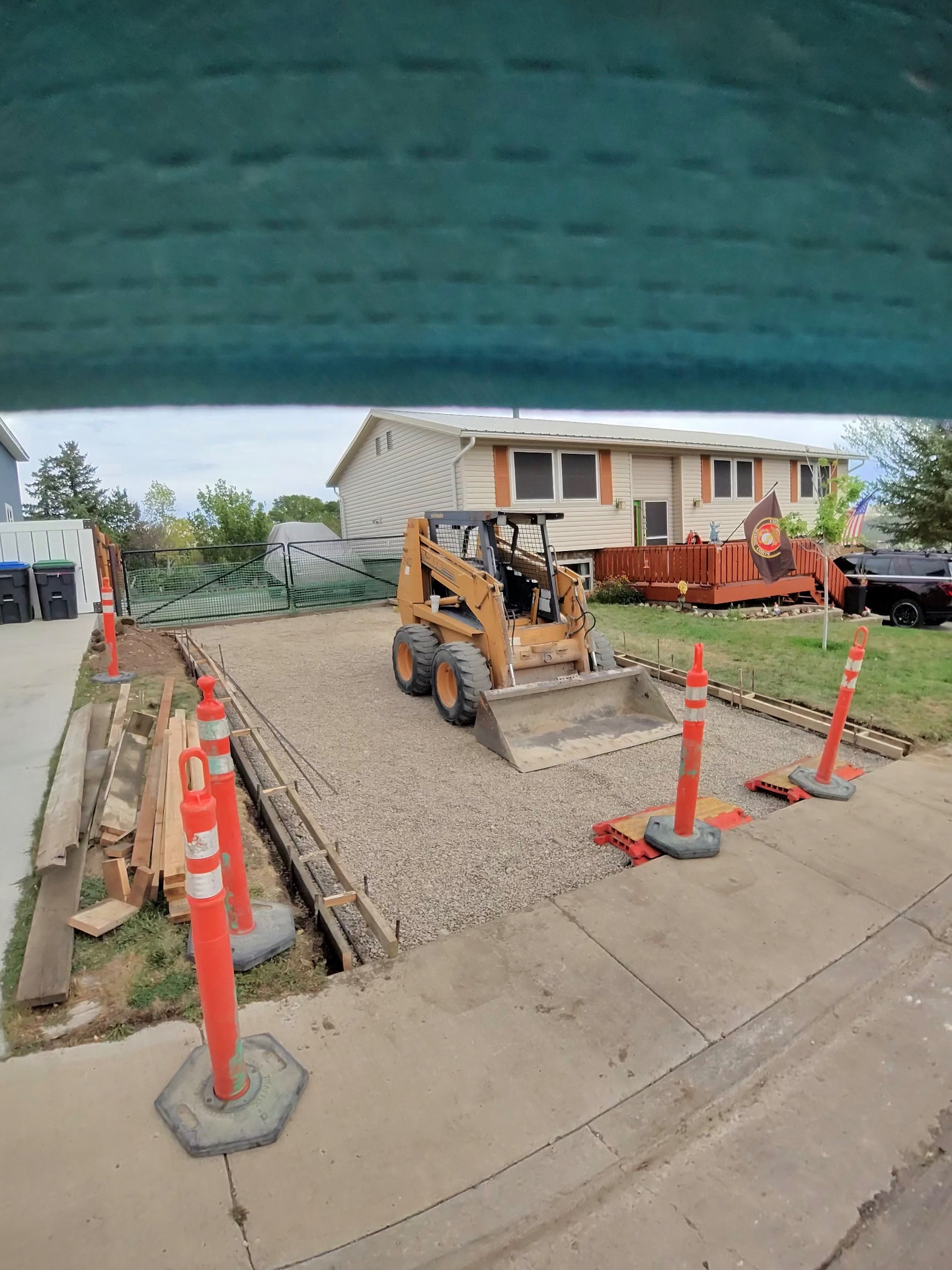Skid steer grading a compacted gravel base inside formed edges for a residential concrete pad.