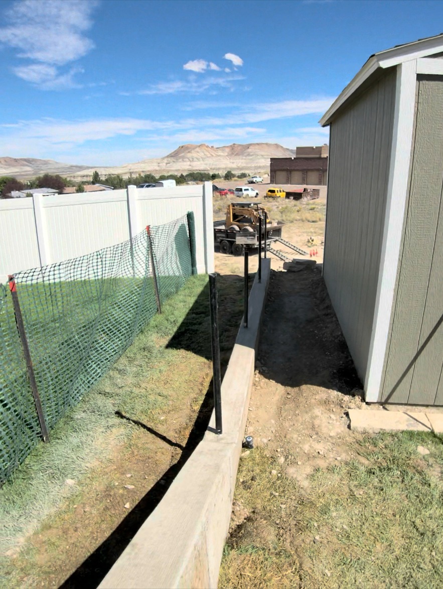 Poured concrete curb and graded side yard running past a storage shed toward open Wyoming terrain.