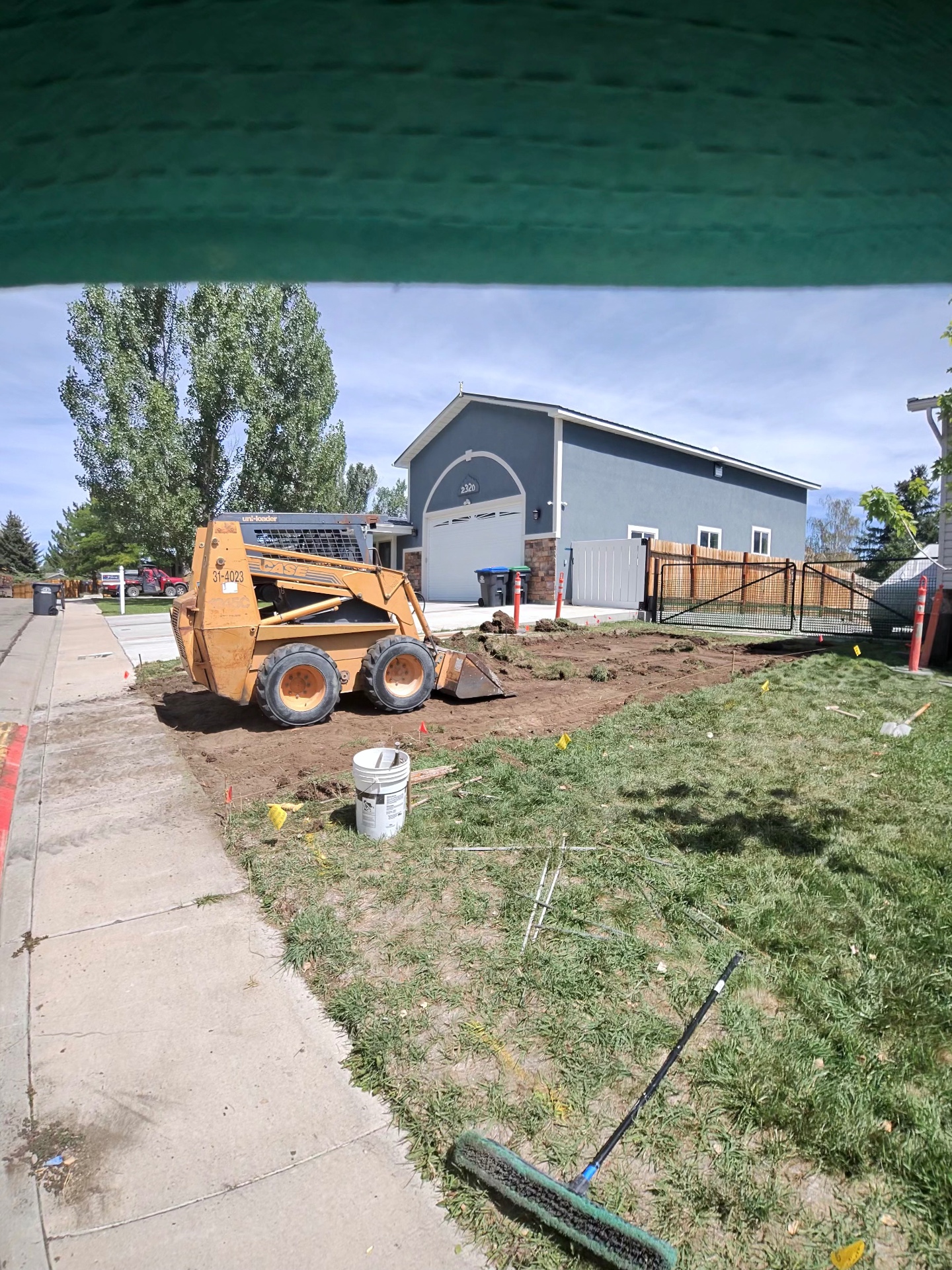 Skid steer stripping sod and grading a residential front yard ahead of new concrete flatwork.