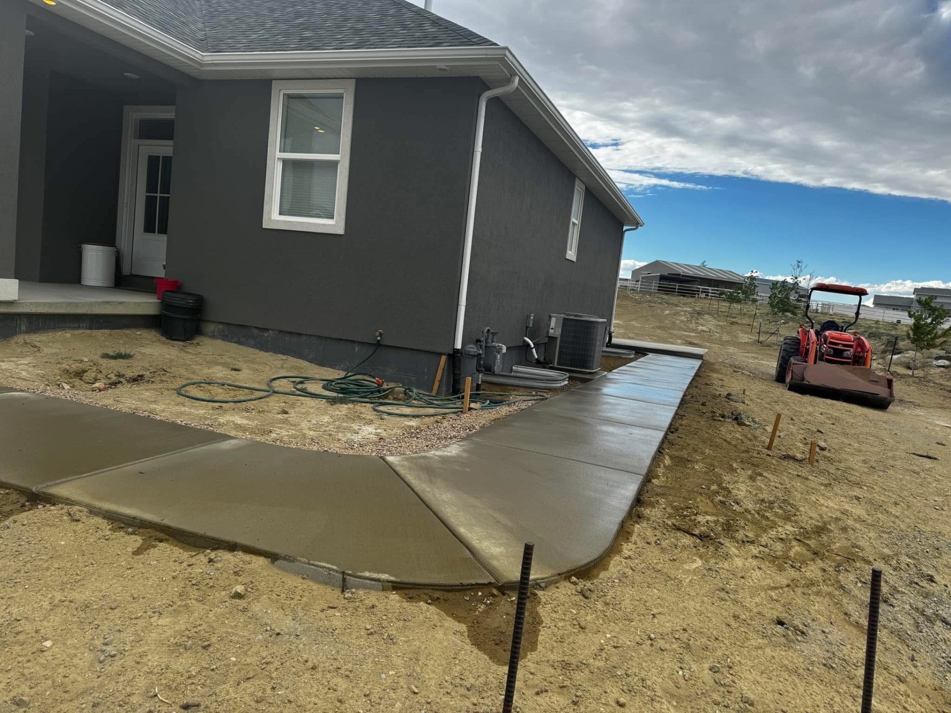 Freshly finished concrete walkway wrapping around the side of a house.