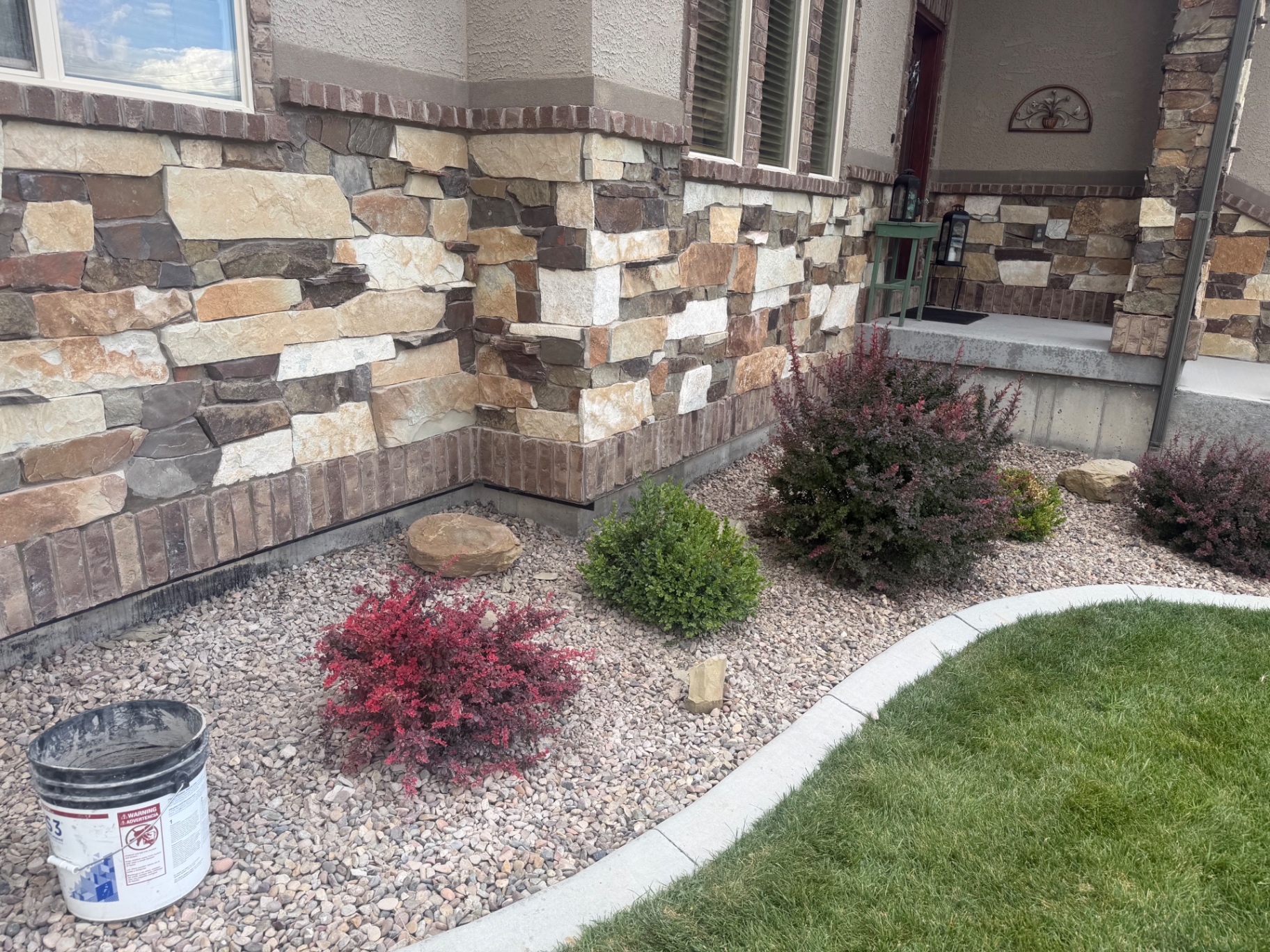 Stone veneer and brick trim along the base of a home beside a curbed rock bed.