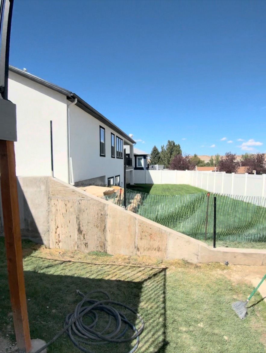 Stepped retaining wall with fresh sod and safety fencing along the side of a home.