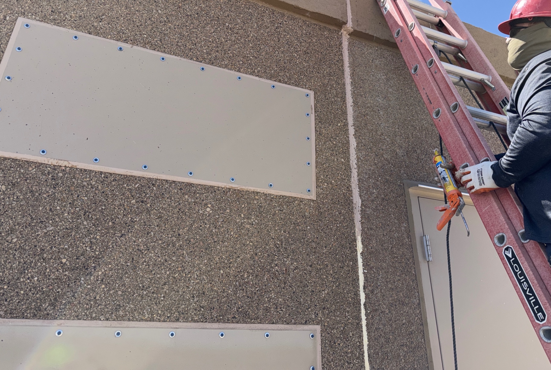 Exterior building sealing work: sealing penetrations and joints with construction sealants and expanding foam on a commercial facility envelope.