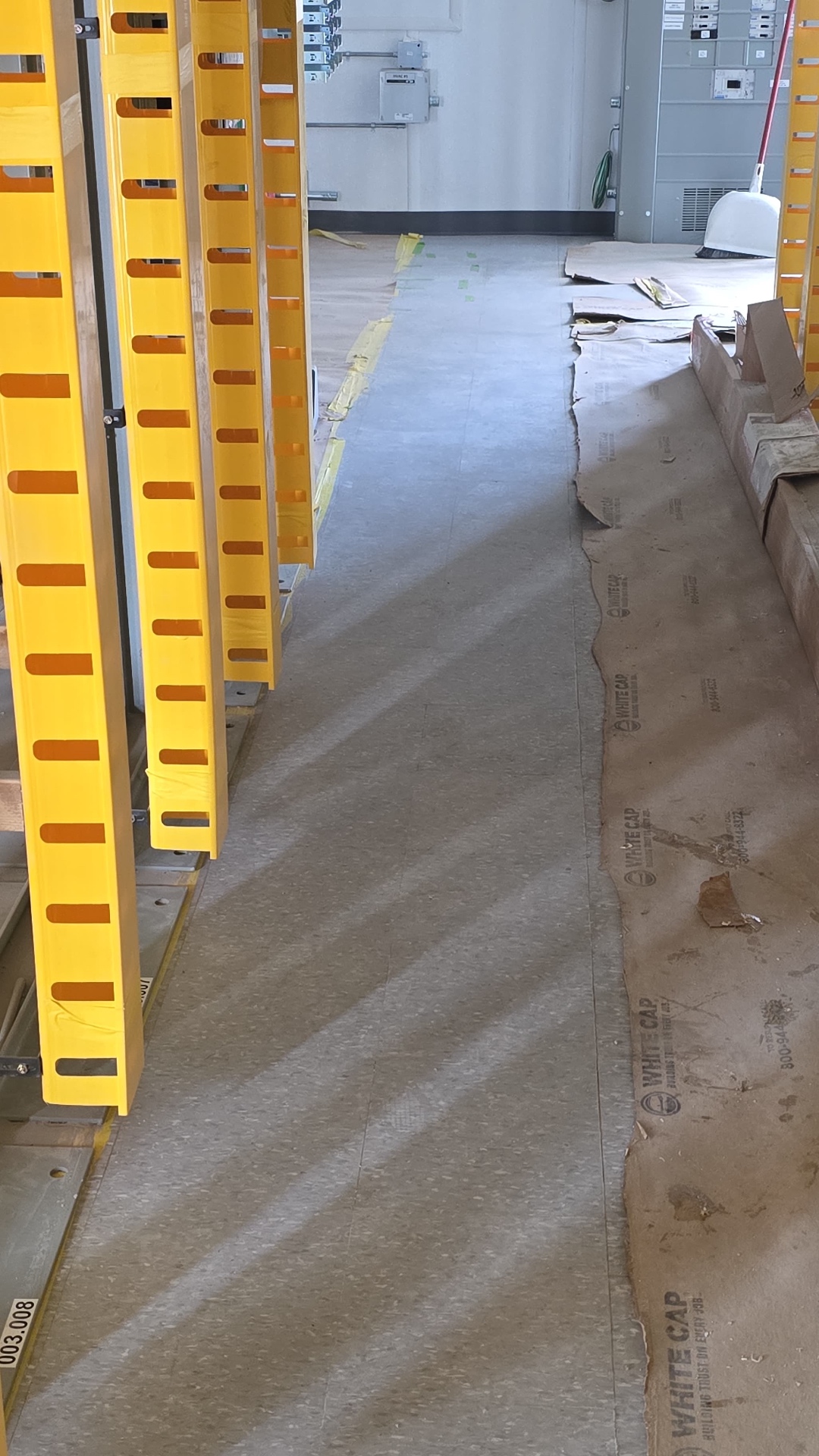 Protected concrete aisle floor alongside yellow equipment framing inside a facility.