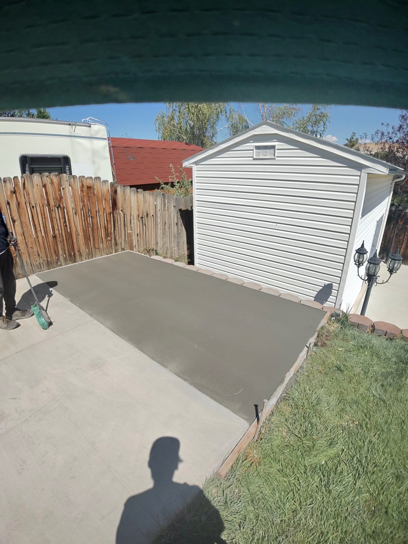 Freshly placed and floated concrete pad alongside a white storage shed.