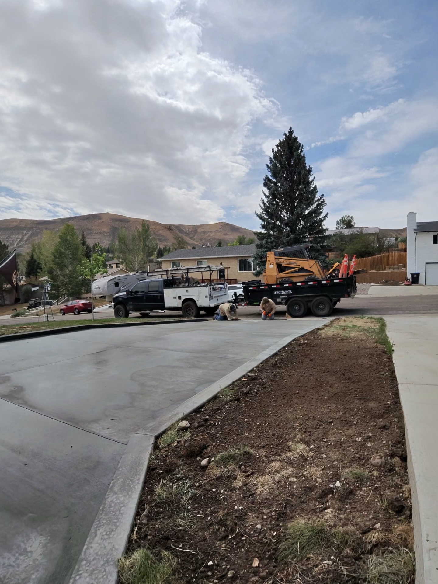 Crew finishing the edge of a freshly placed concrete driveway with equipment staged at the street.