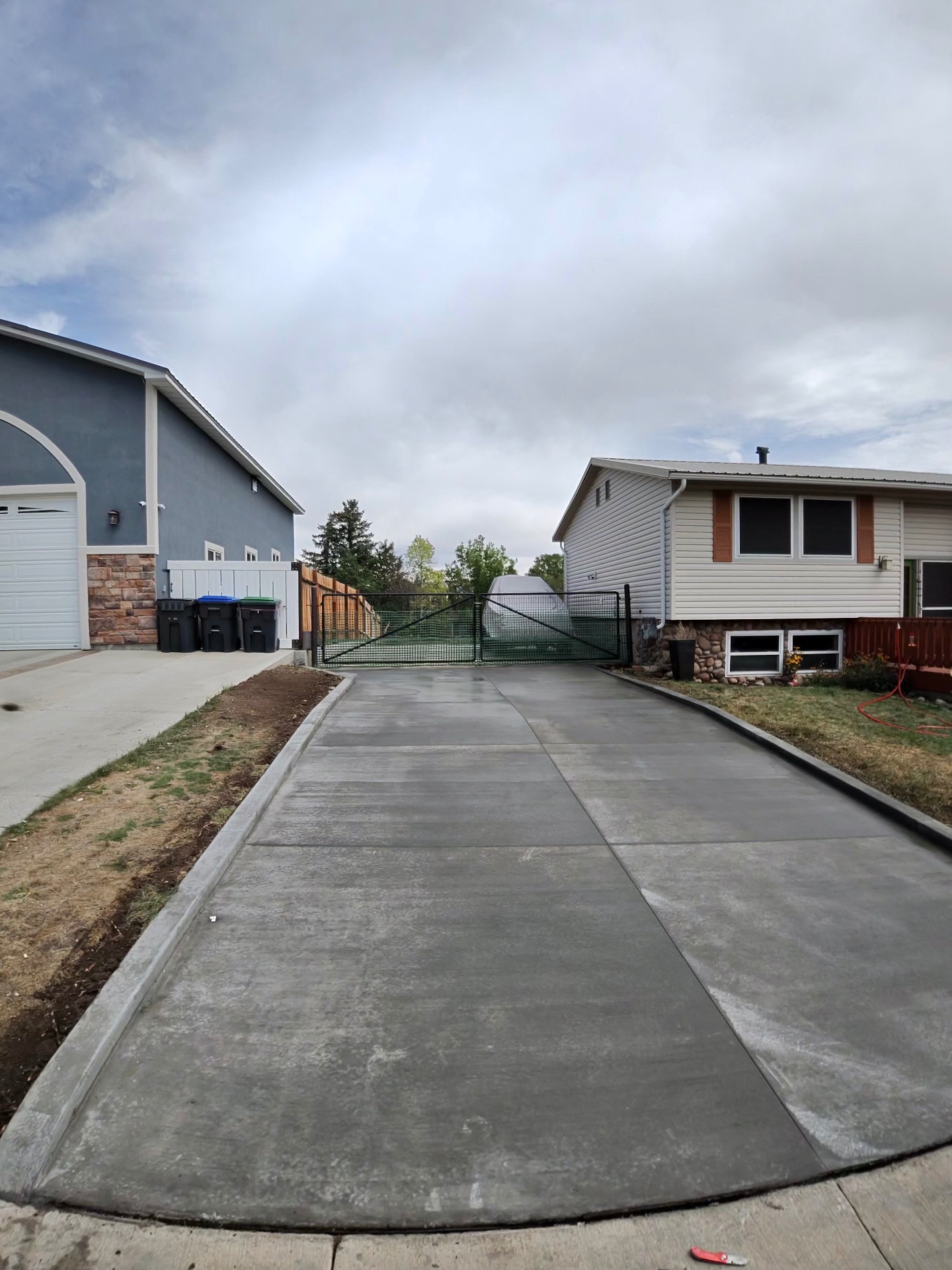 Long finished concrete driveway running between two homes to a rear gate.