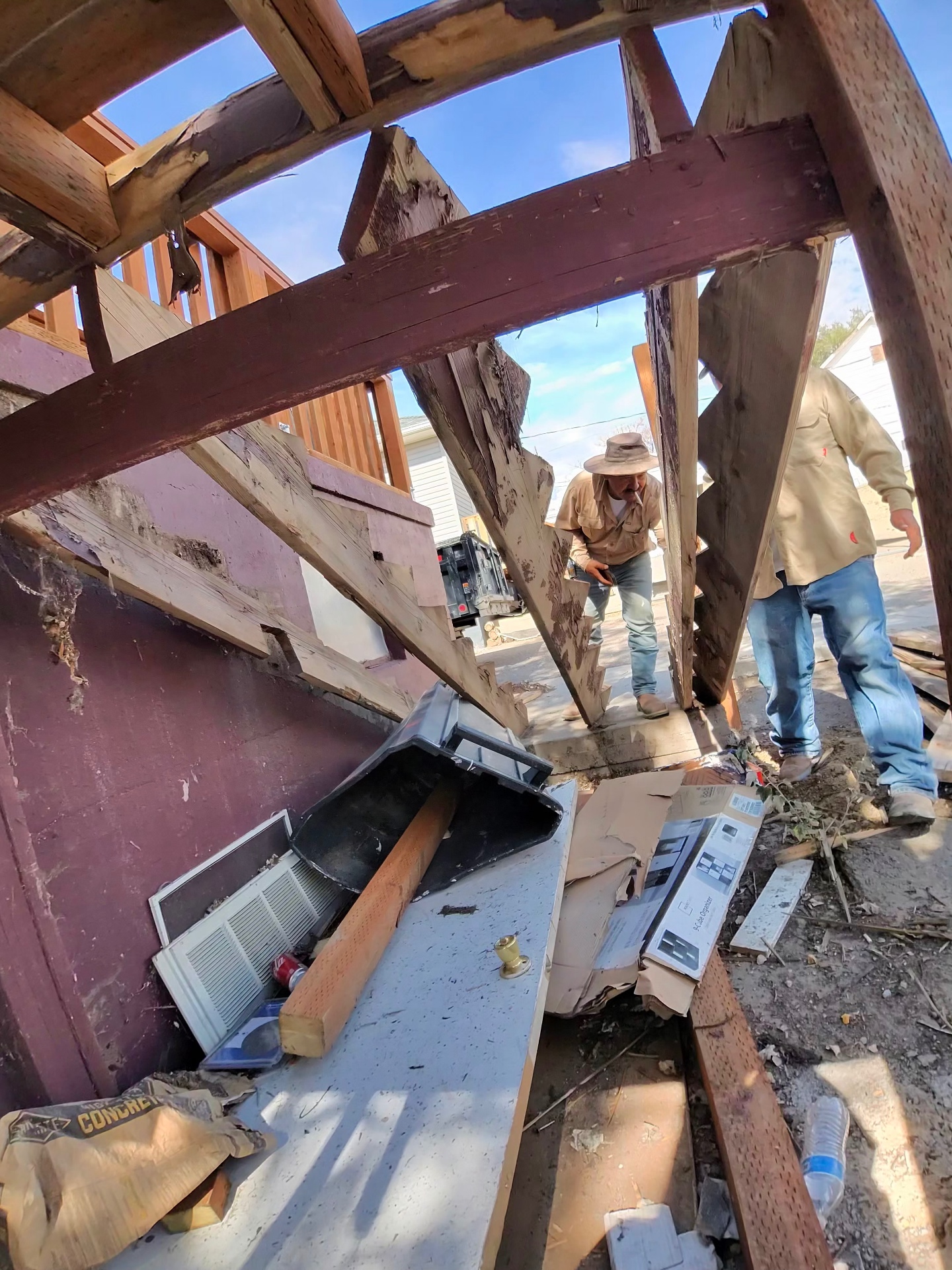 Crew members removing framing and debris during demolition of an exterior structure.