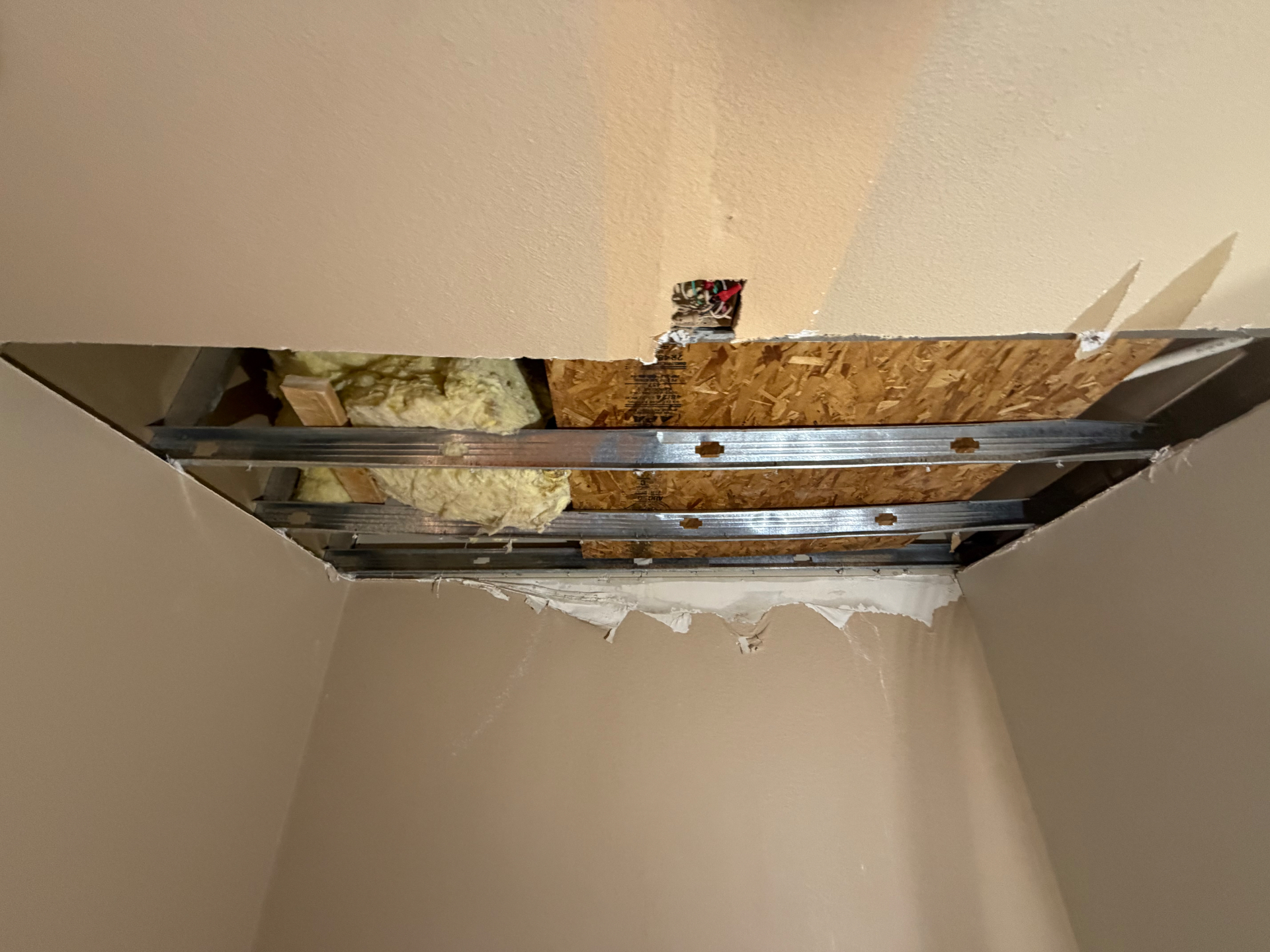 Opened interior ceiling showing metal framing, insulation and sheathing above.
