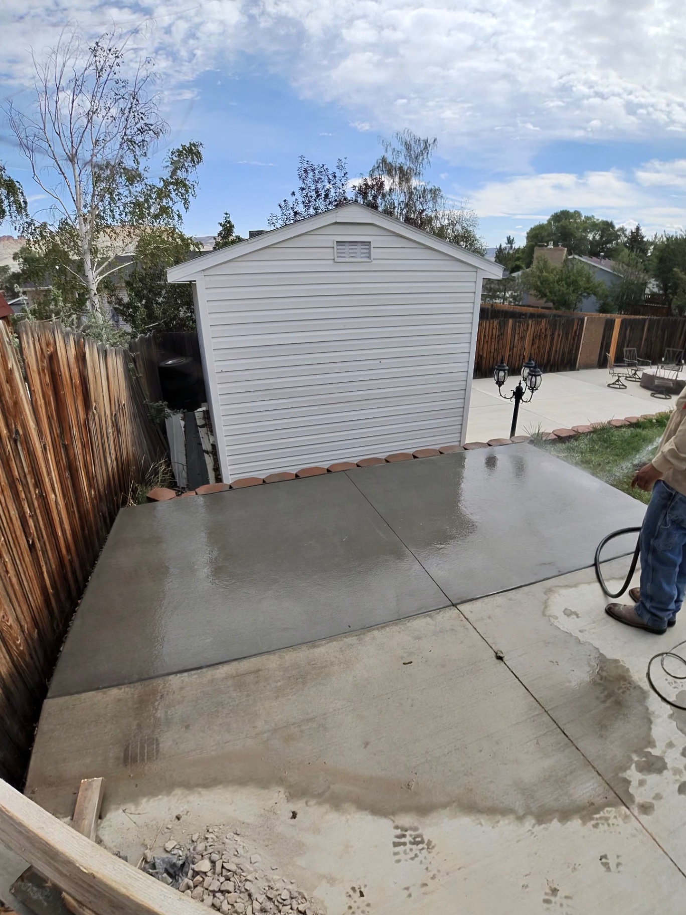 Finished backyard concrete slab being wet-cured next to a storage shed and patio.